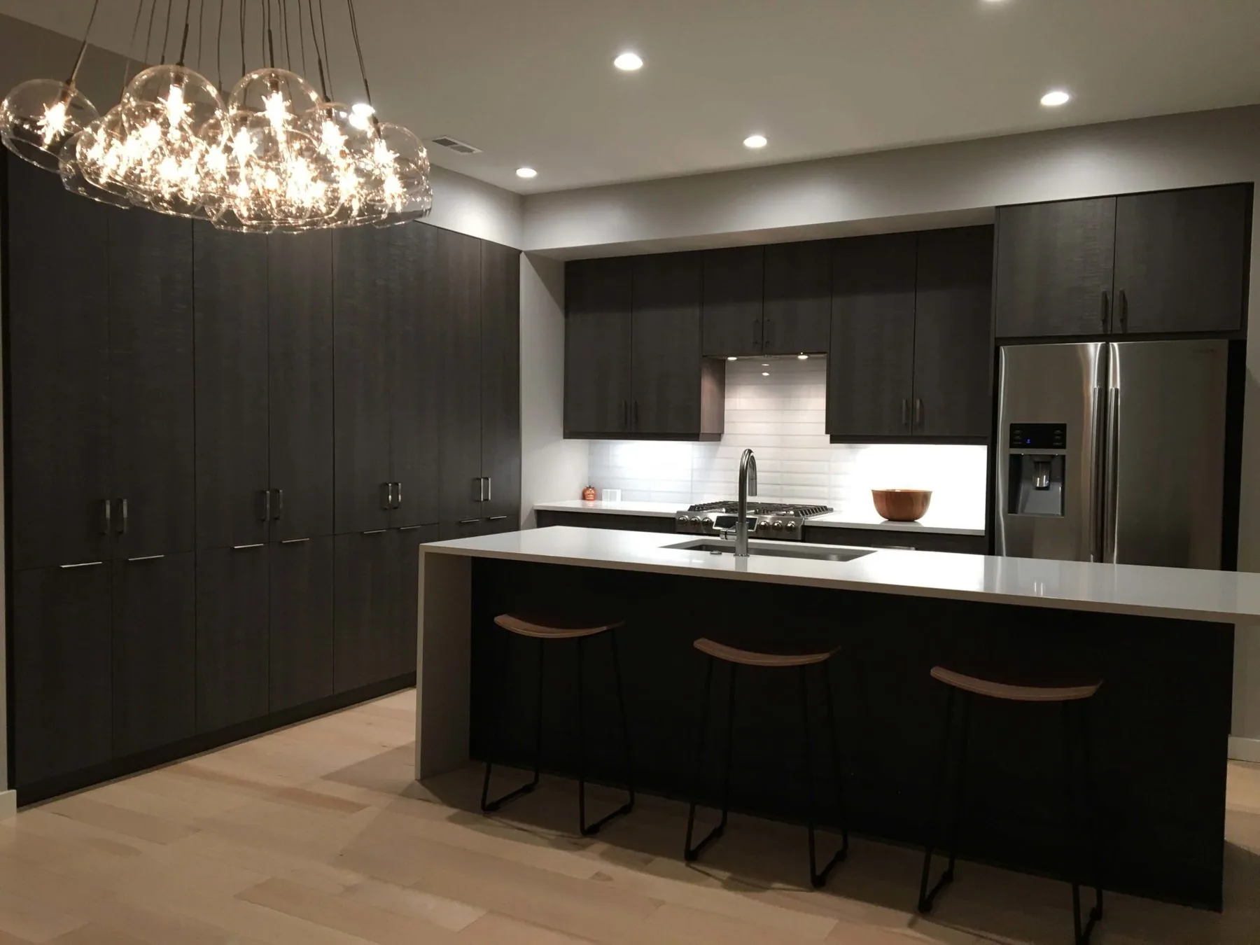 Dark custom kitchen by Sarasota Kitchen Company with island seating and pendant lighting